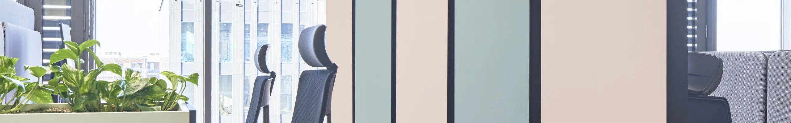 Modern office space with suspended pastel acoustic panels, workstation pods, plant-filled modular partitions, and a white grid acoustic ceiling.