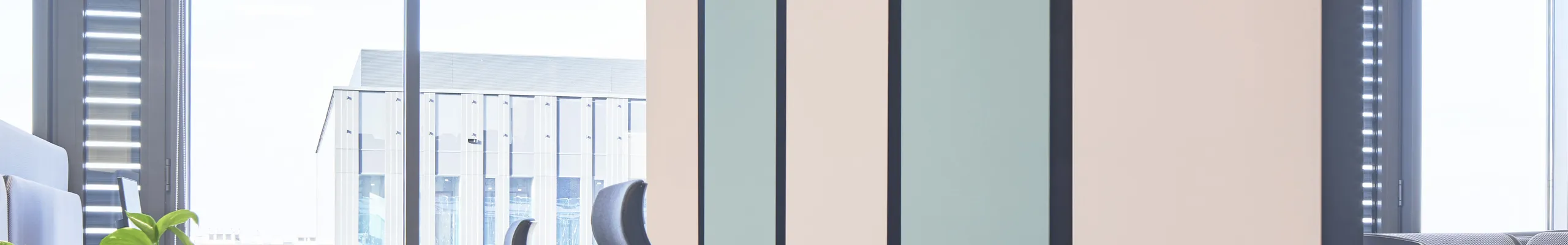 Modern office space with suspended pastel acoustic panels, workstation pods, plant-filled modular partitions, and a white grid acoustic ceiling.