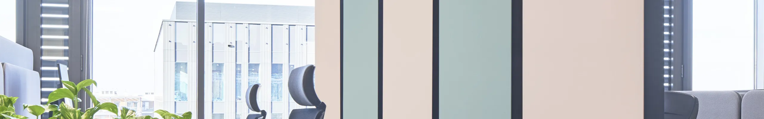 Modern office space with suspended pastel acoustic panels, workstation pods, plant-filled modular partitions, and a white grid acoustic ceiling.