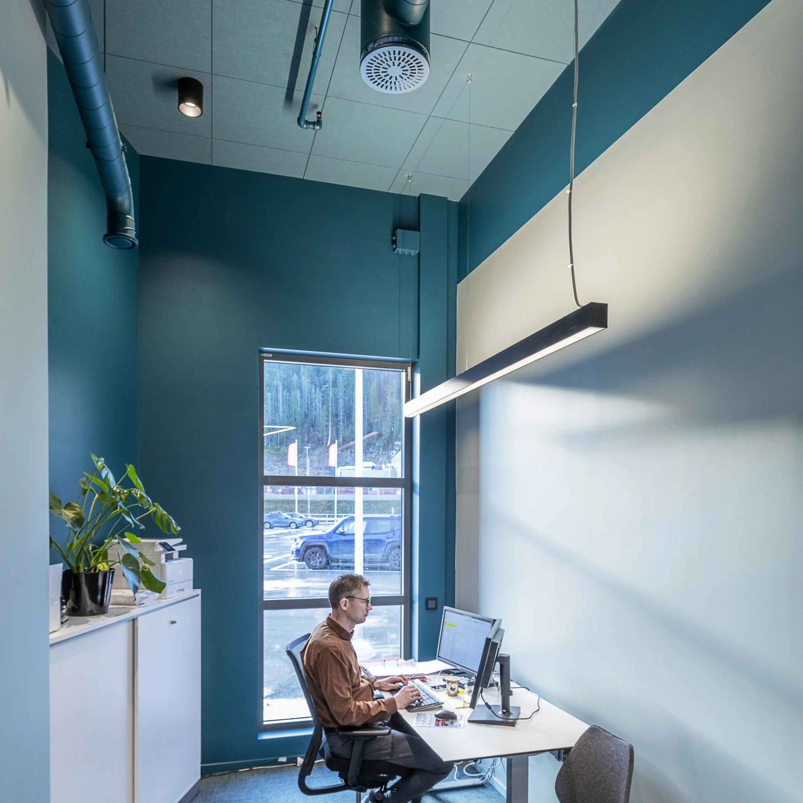 Man working at a desk in a small office with coloured acoustic ceiling panels and exposed ventilation ducts