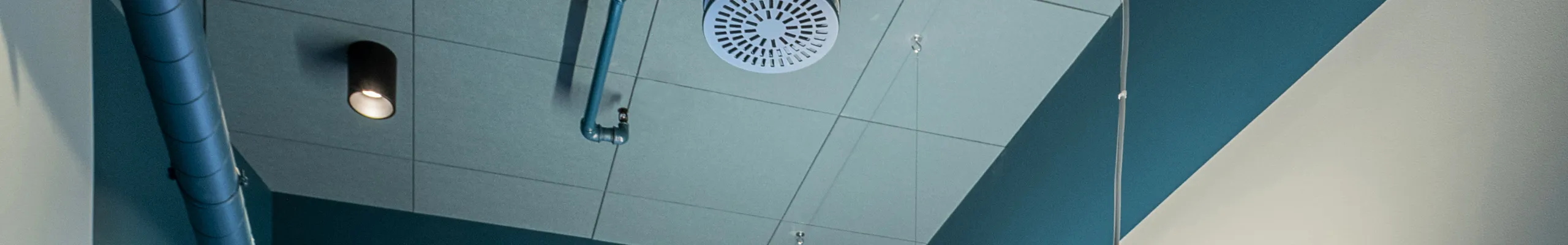 Contemporary single-person office featuring teal accent walls, high ceiling with exposed ducts, large window, and minimalist workstation setup