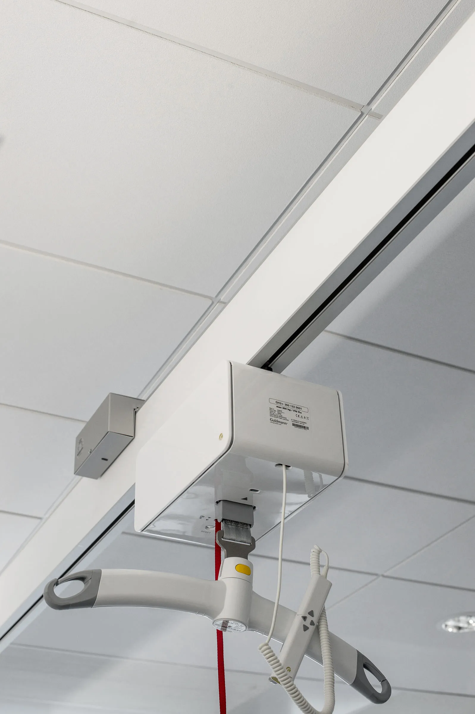 A close-up view of a ceiling-mounted patient hoist system installed within a smooth, wipe-clean acoustic ceiling tile grid.