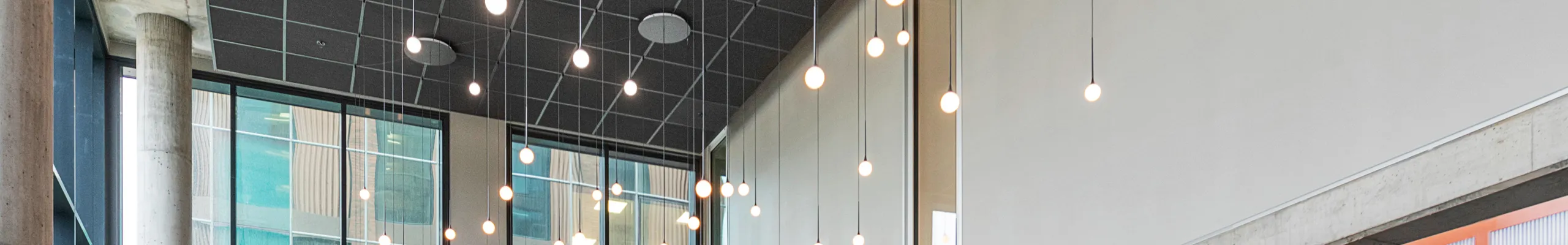 Modern office breakout area interior with high ceilings, black acoustic panels, hanging pendant lights, round tables with burgundy seating, and a bar area with wooden stools and green tiles