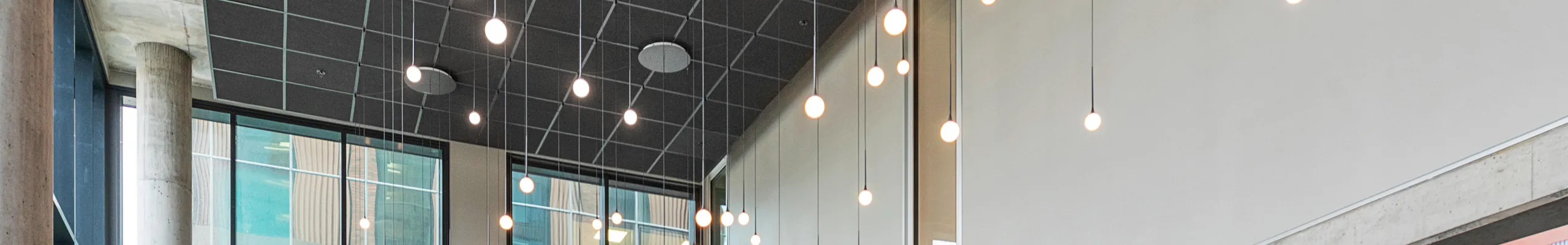 Modern office breakout area interior with high ceilings, black acoustic panels, hanging pendant lights, round tables with burgundy seating, and a bar area with wooden stools and green tiles