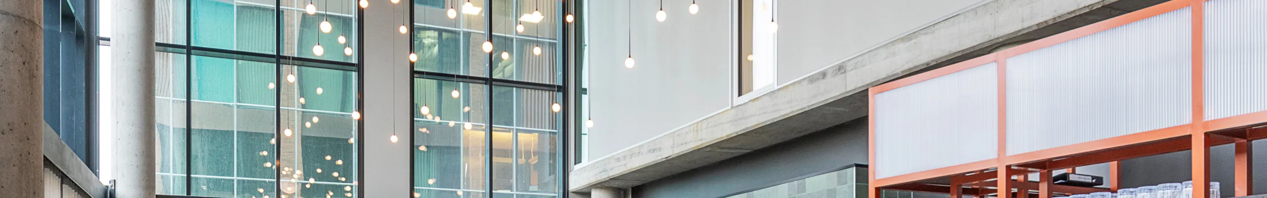 Modern office breakout area interior with high ceilings, black acoustic panels, hanging pendant lights, round tables with burgundy seating, and a bar area with wooden stools and green tiles