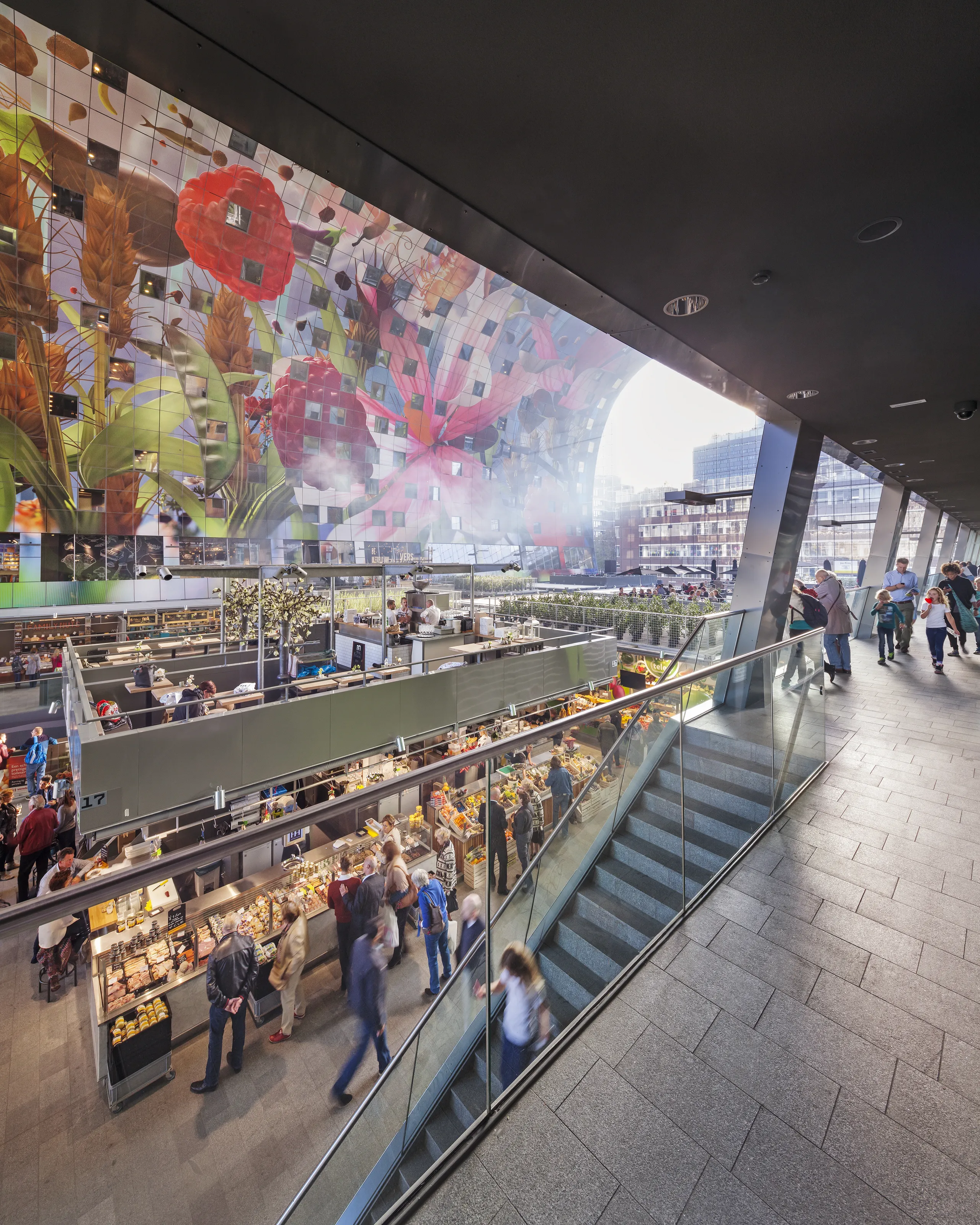 Interior view of Markthal Rotterdam with food market stalls, visitors, and the large colourful ceiling artwork spanning the vaulted structure.
