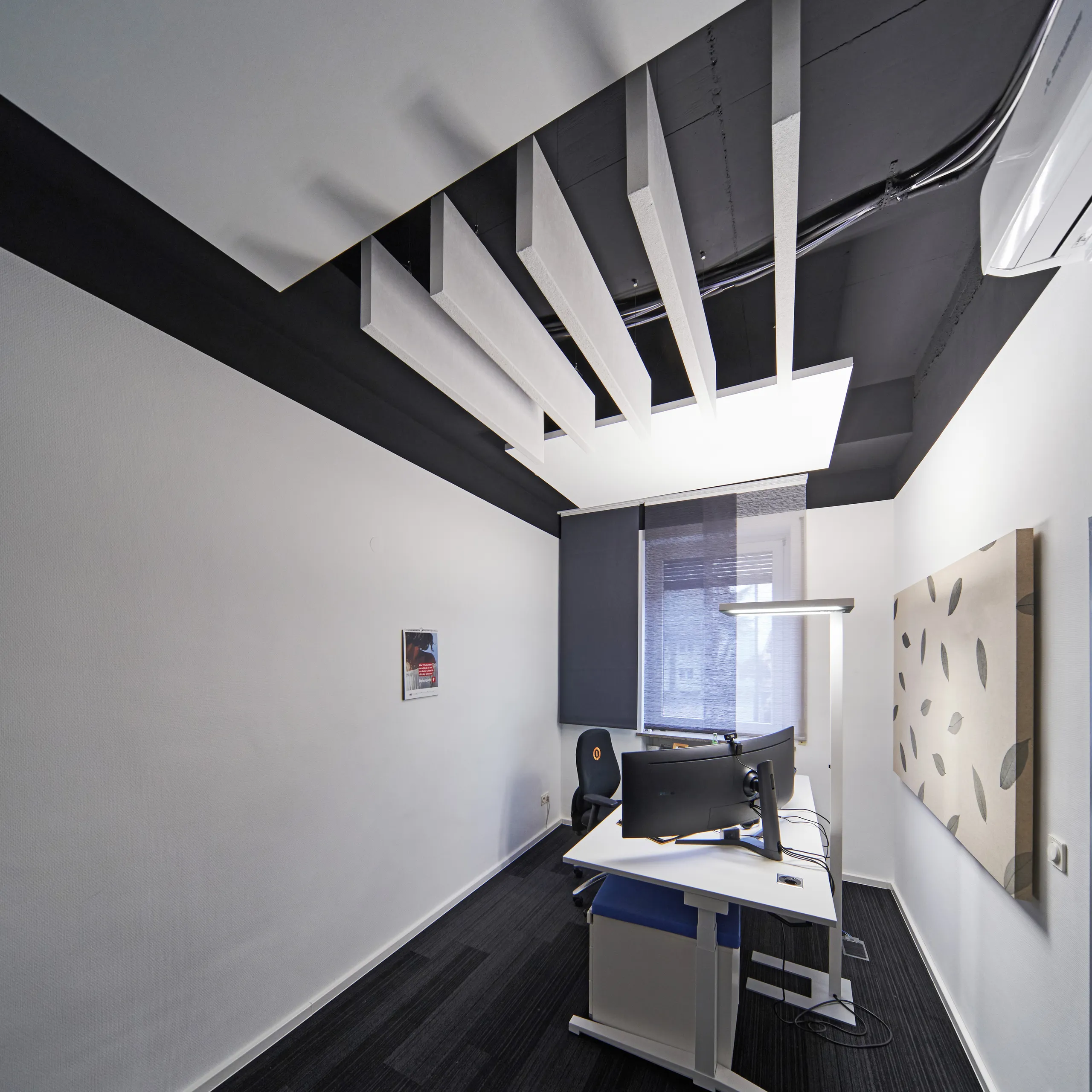 Compact workspace featuring vertical white acoustic baffles installed across a black acoustic ceiling tiles and acoustic wall panels featuring natural leavesto improve sound absorption.