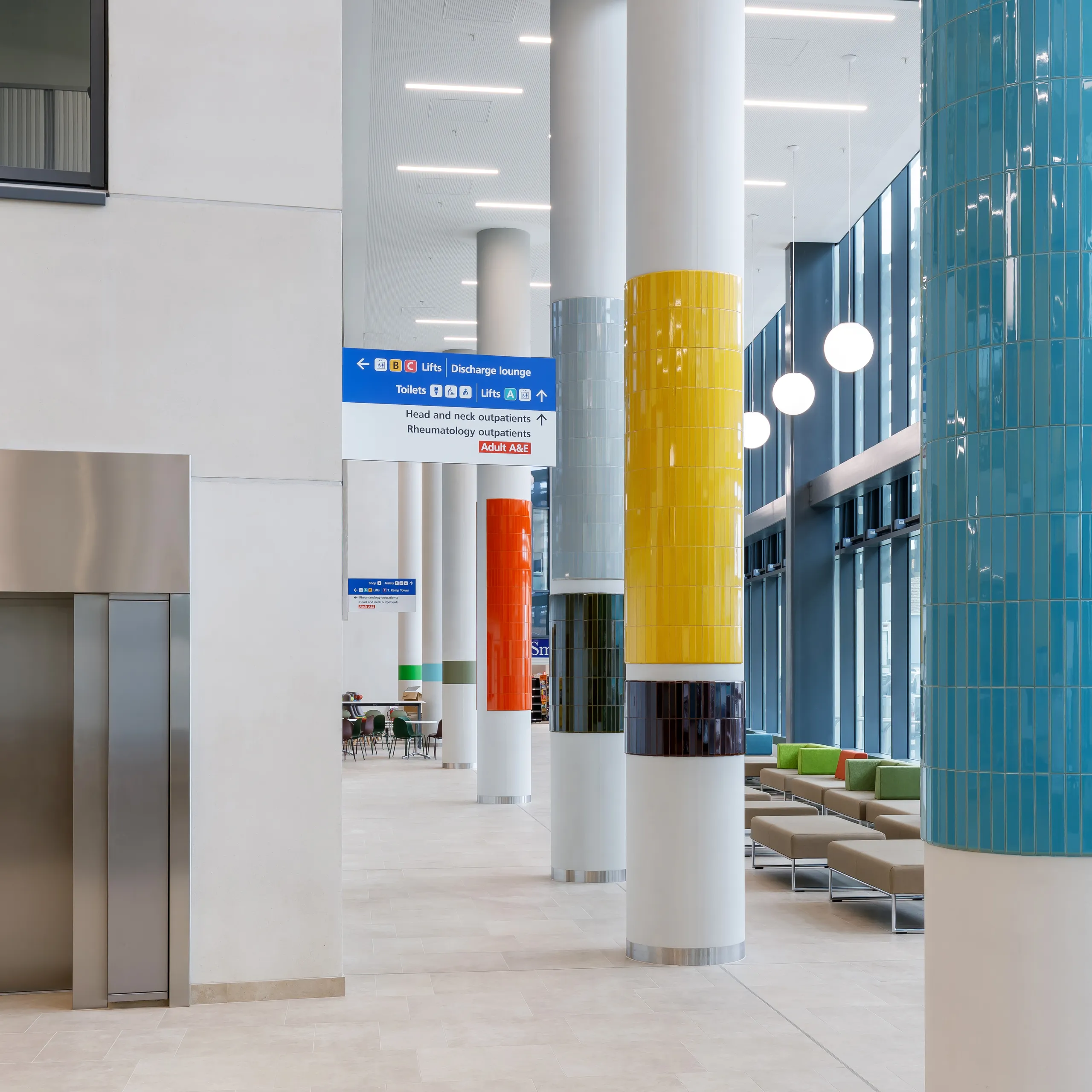 Multicoloured tiled pillars and modern seating in a bright hospital lobby with high ceilings and large windows.