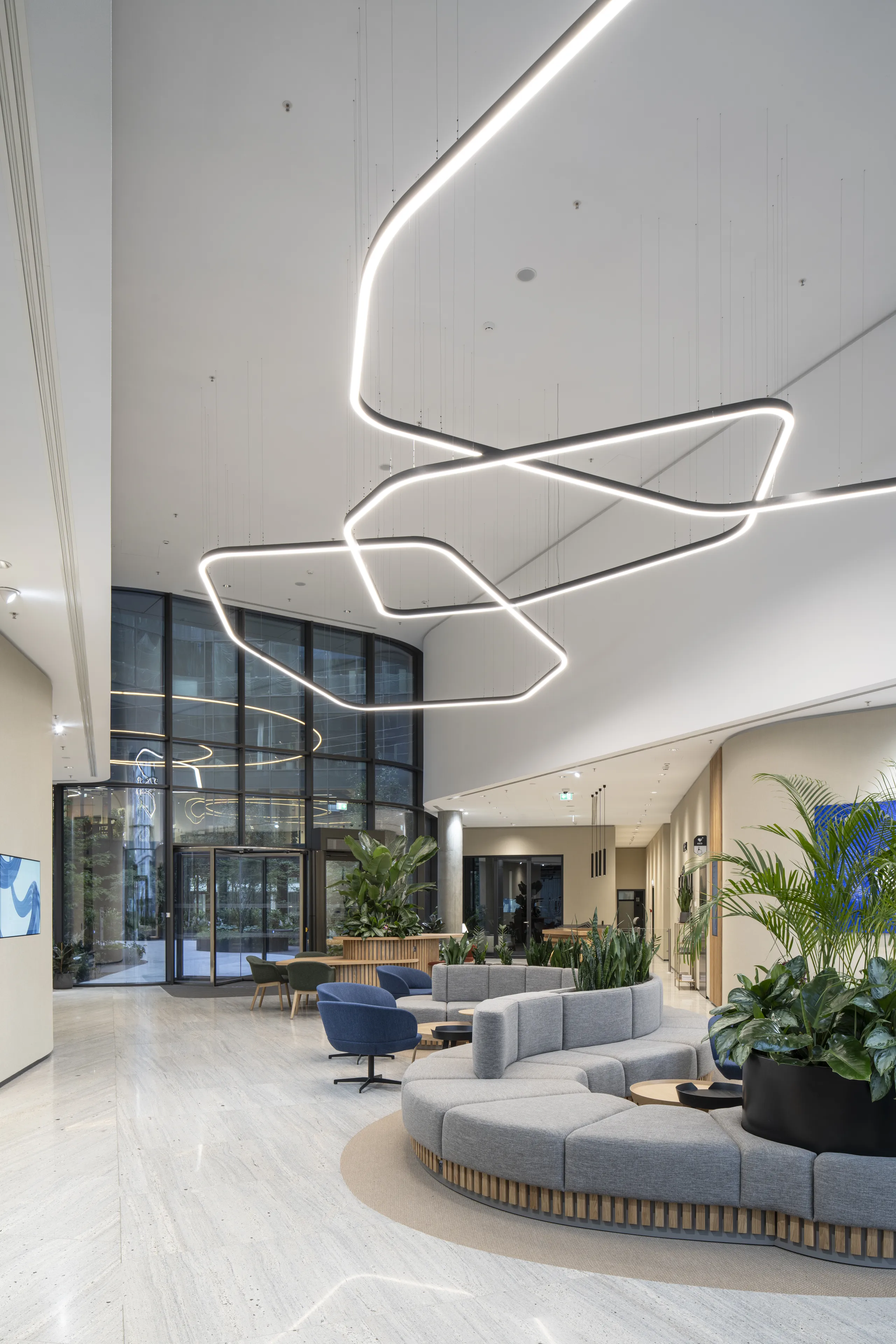 Elegant reception area with a smooth monolithic acoustic ceiling, suspended sculptural light installation, curved lounge seating, and abundant indoor planting