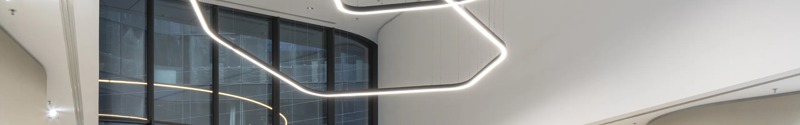 Elegant reception area with a smooth monolithic acoustic ceiling, suspended sculptural light installation, curved lounge seating, and abundant indoor planting