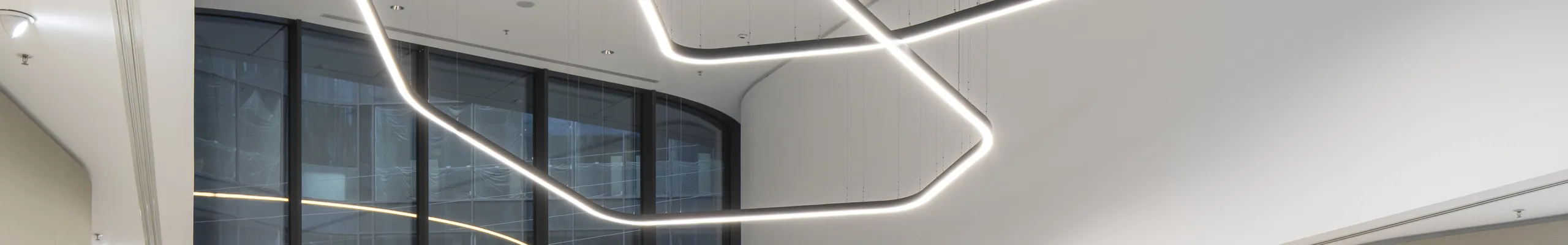 Elegant reception area with a smooth monolithic acoustic ceiling, suspended sculptural light installation, curved lounge seating, and abundant indoor planting