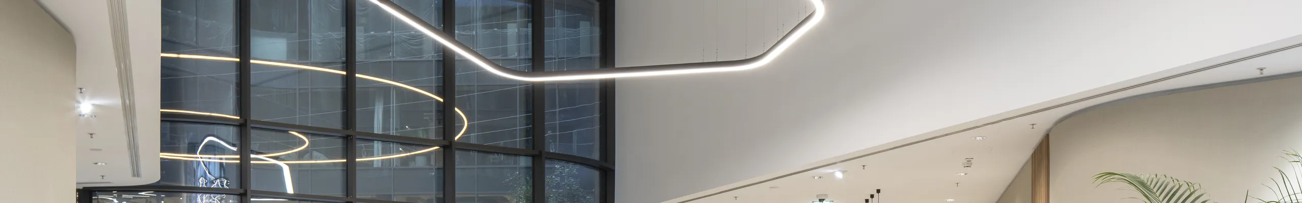 Elegant reception area with a smooth monolithic acoustic ceiling, suspended sculptural light installation, curved lounge seating, and abundant indoor planting