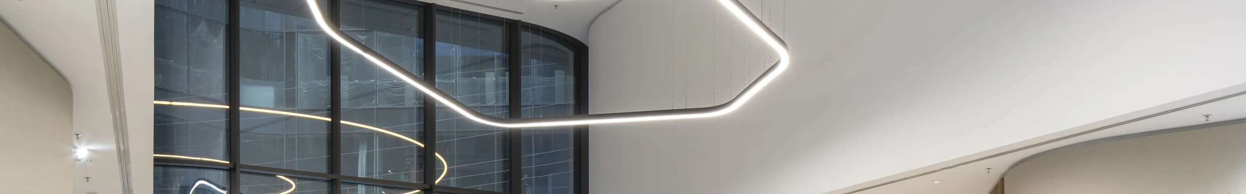 Elegant reception area with a smooth monolithic acoustic ceiling, suspended sculptural light installation, curved lounge seating, and abundant indoor planting