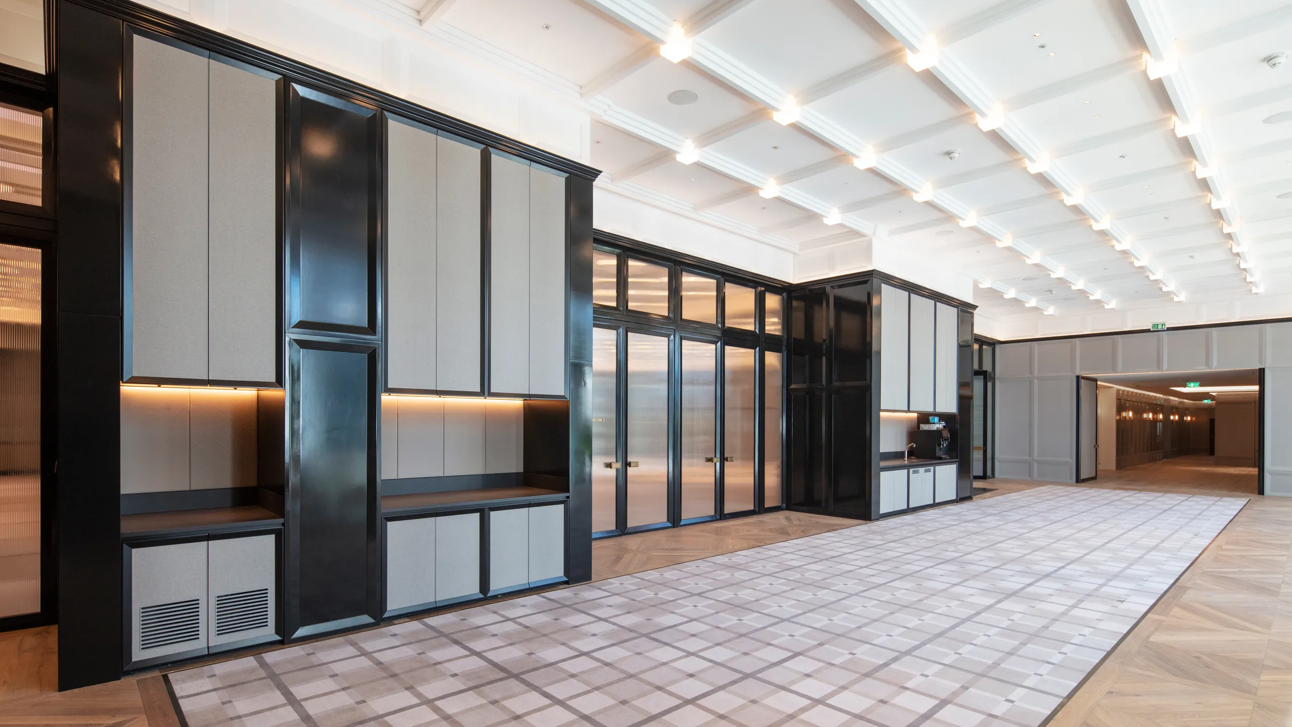 Luxury hotel lobby with reception desk, large artwork, sculptural lighting installation, and a white coffered acoustic ceiling above the space.