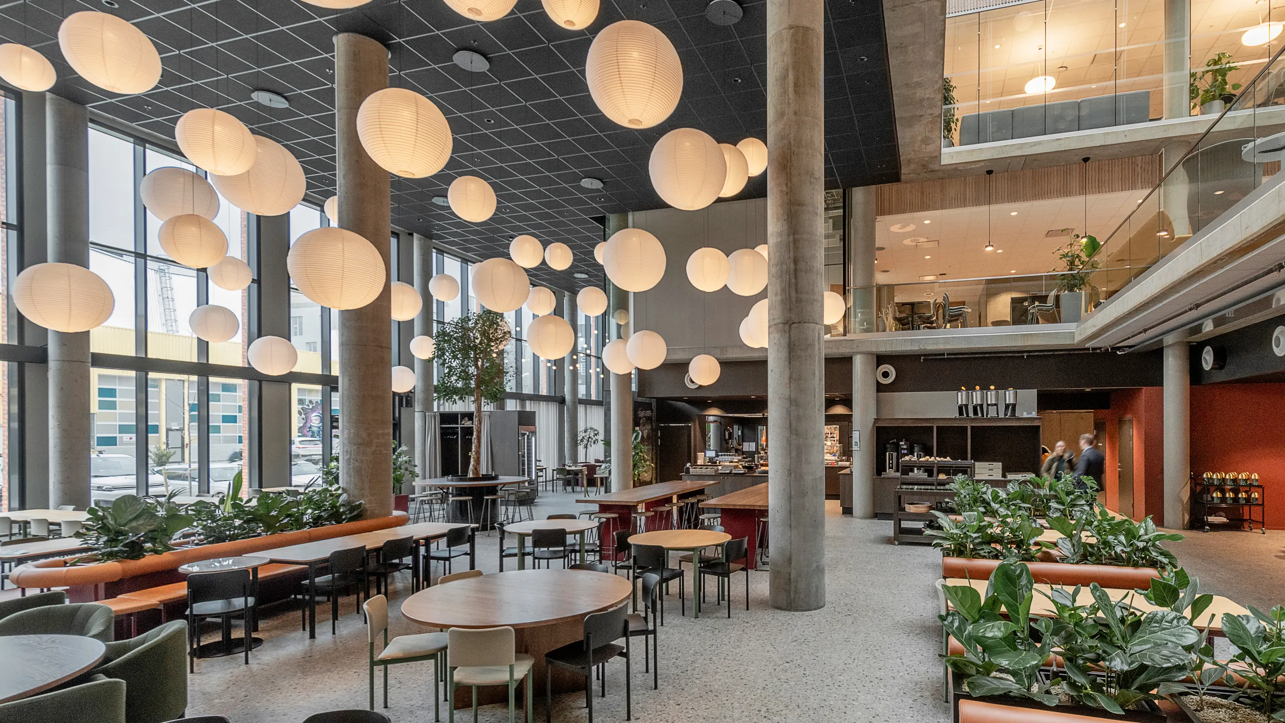 Office atrium with black suspended ceiling, seating areas, pendant globe lighting, and a black acoustic grid ceiling installed beneath a mezzanine level.