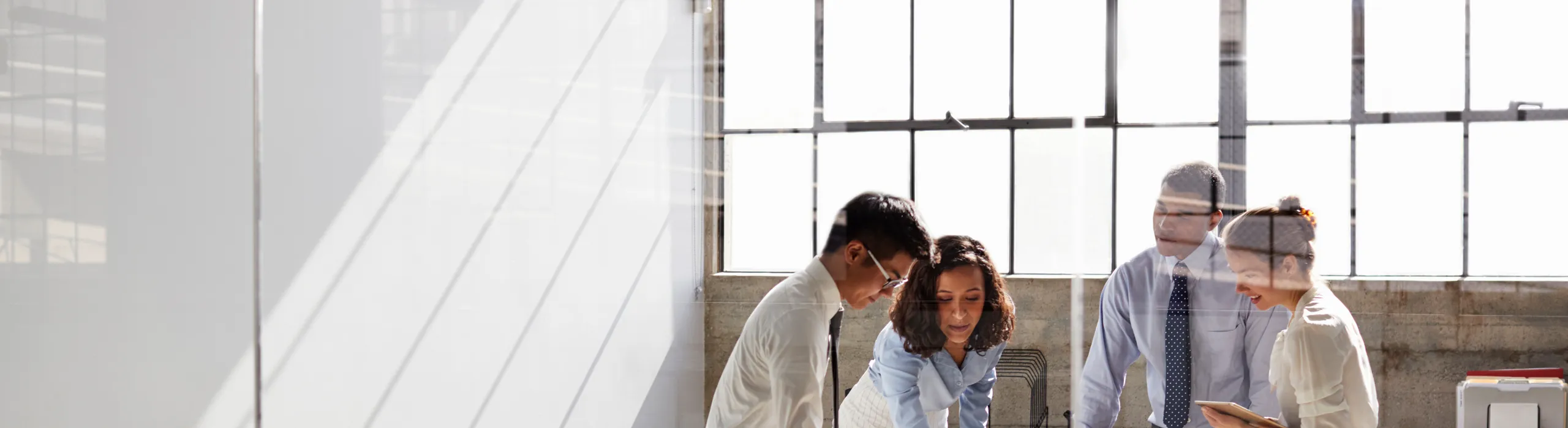 Modern office meeting with four professionals working together at a table in a loft-style room with tall steel-framed windows