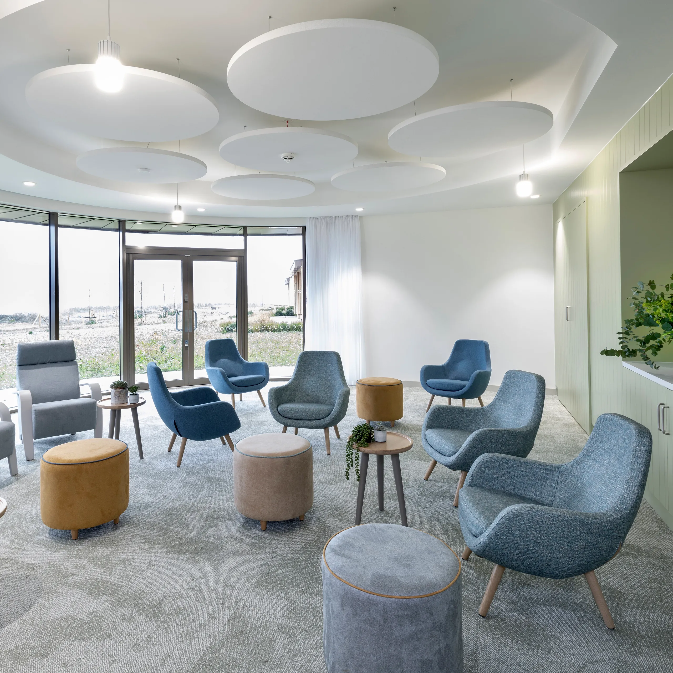 A calm, light-filled lounge with soft seating arranged in a circle and large white circular acoustic rafts suspended from the ceiling.