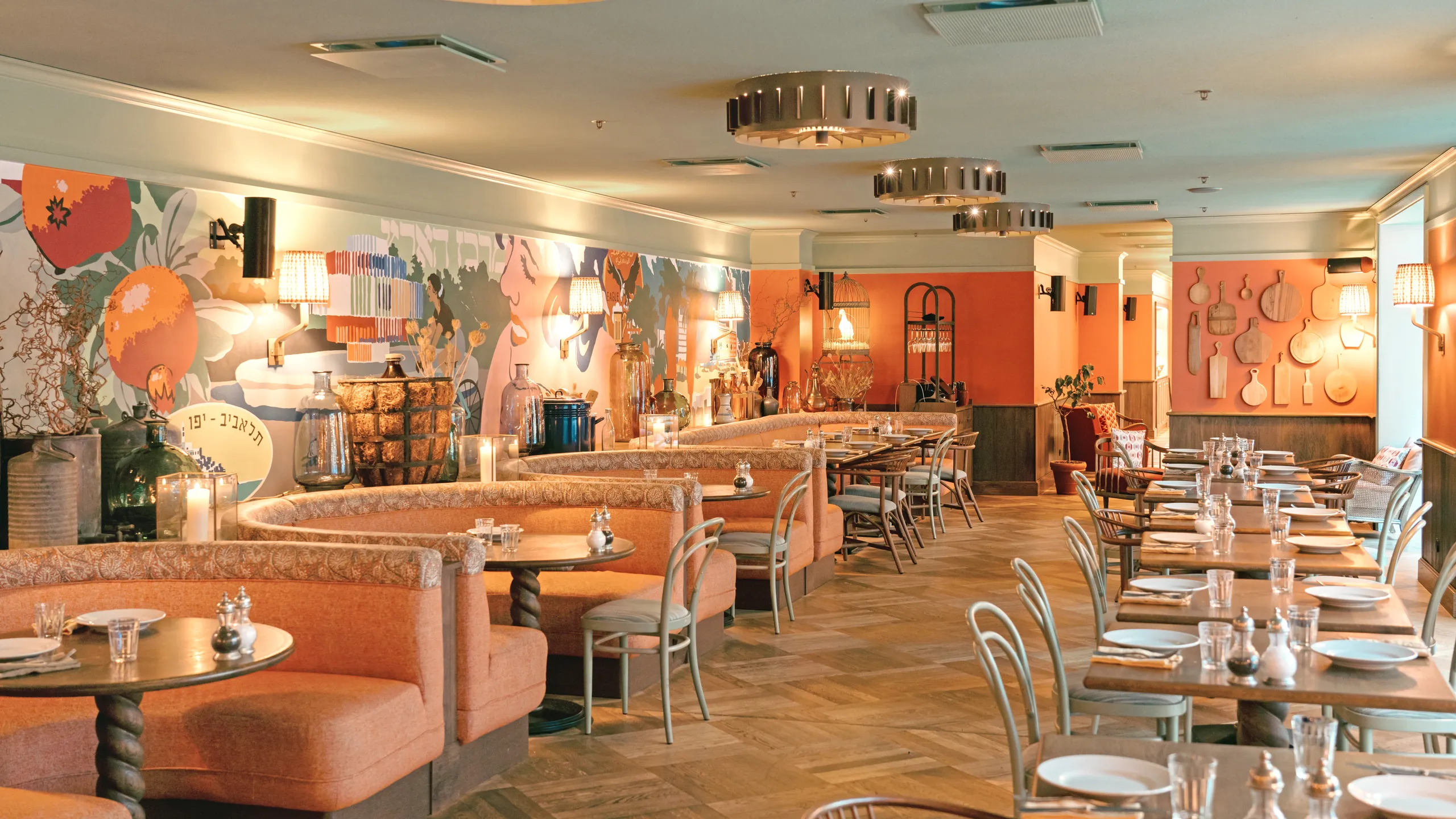 Stylish restaurant interior with orange walls, patterned booths, wooden tables, chairs, decorative wall art, and ambient lighting.