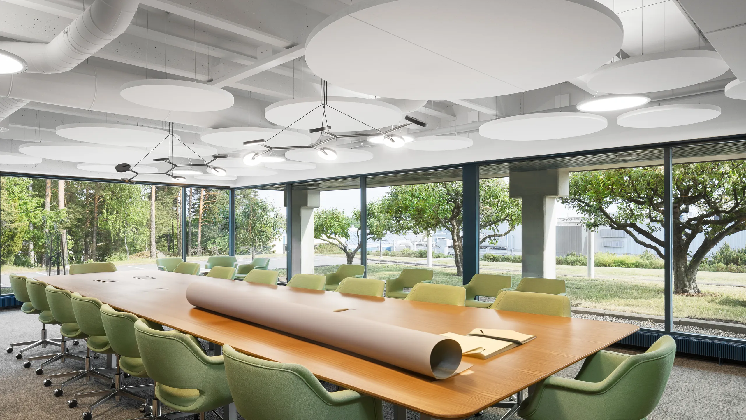 Modern conference room with a long wooden table, green swivel chairs, large windows, and circular ceiling lights and white floating office ceiling, overlooking a garden.