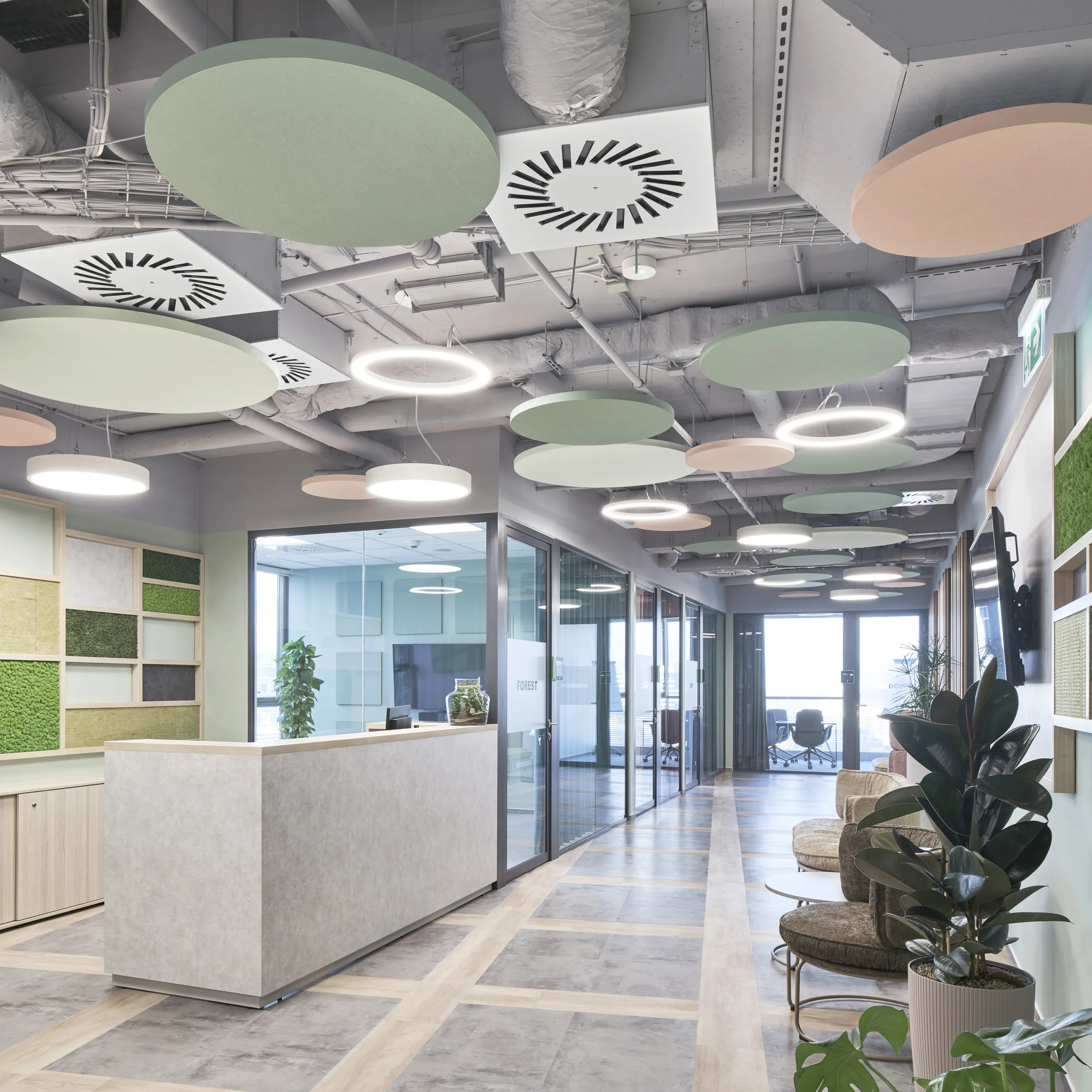 Reception area with suspended circular acoustic islands in pastel colours, exposed ceiling services, and biophilic wall panels beside a modern front desk