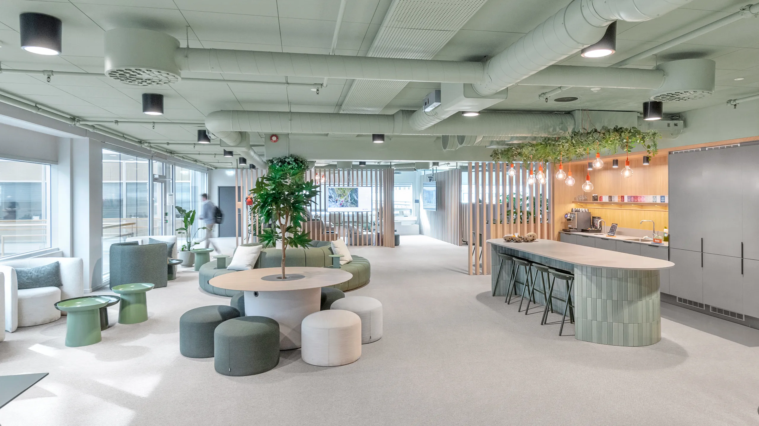 Modern green office ceiling with pastel green decor, round tables, cushioned stools, a long counter with bar stools, and large windows.