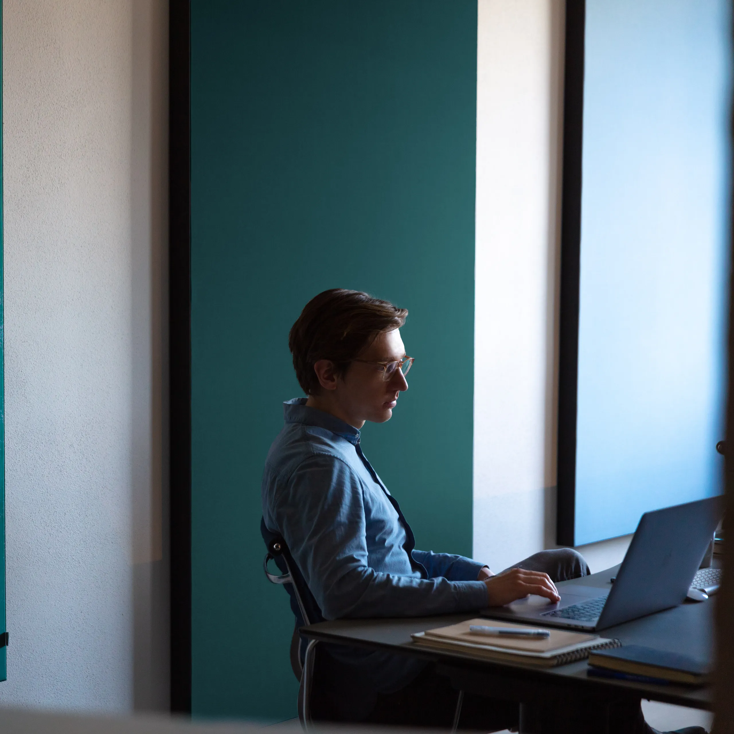 Person working at a laptop in front of large coloured acoustic wall panels, with a printed acoustic panel showing an aerial view of shipwrecks on the left.