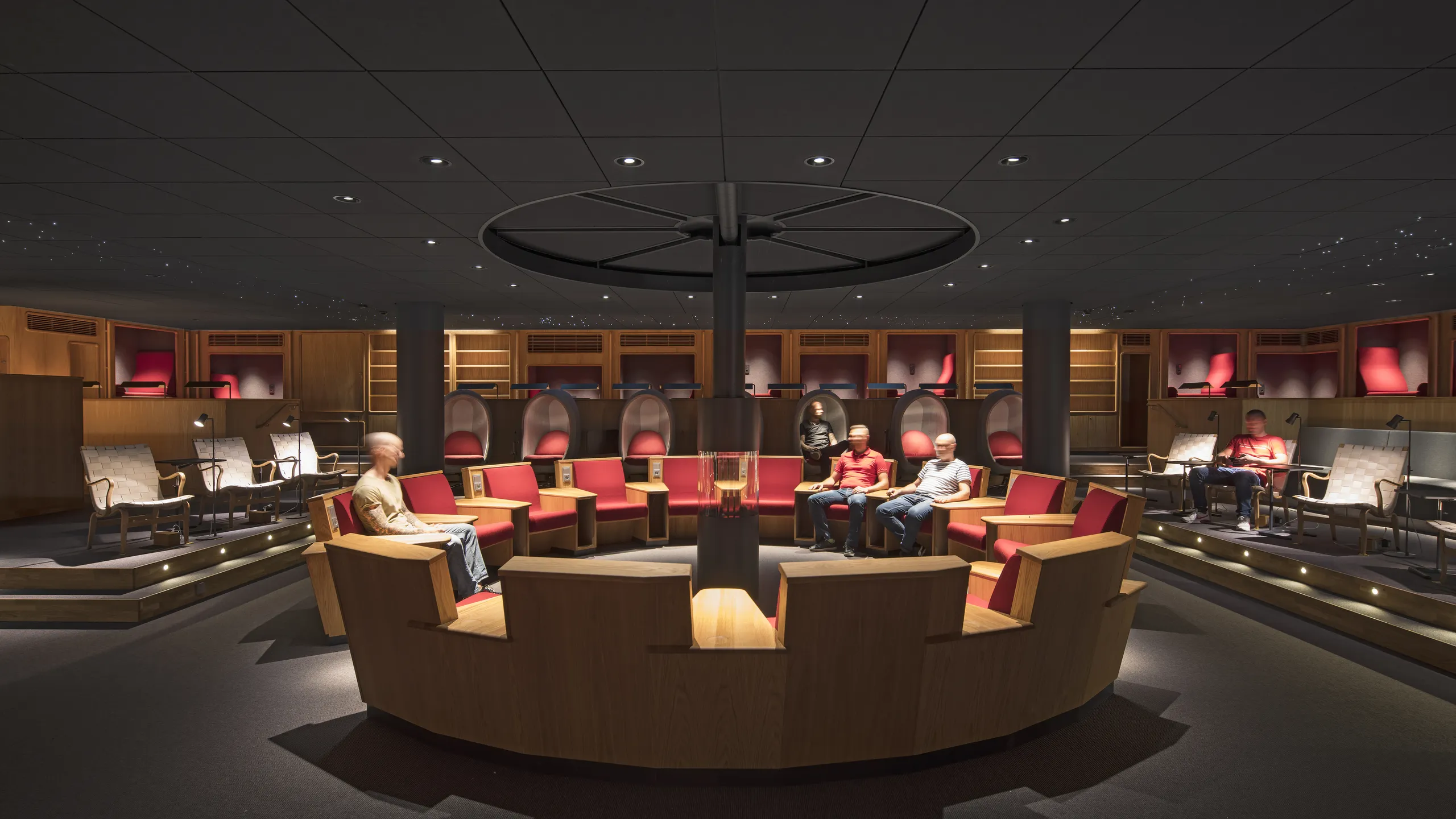 A modern conference room with black suspended ceiling and starry lighting, circular seating, red accents, and dim lighting. People are seated around the room.