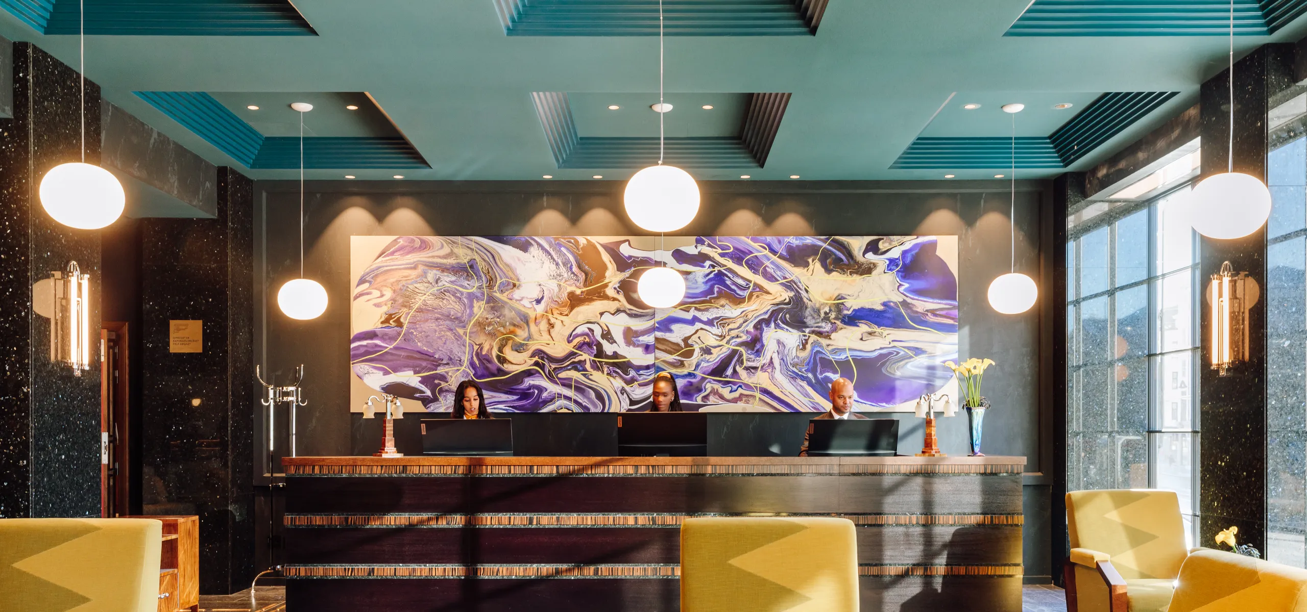 Hotel reception lobby with seating area, front desk, and coloured acoustic ceiling panels with recessed lighting above the space.