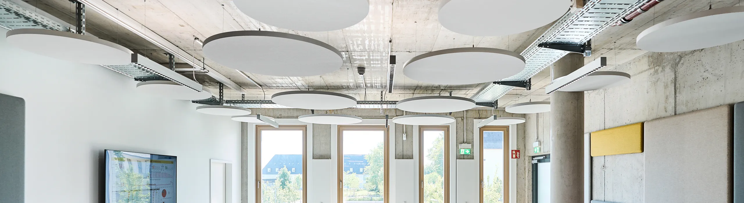 Modern breakout room featuring round acoustic islands on an exposed concrete ceiling, soft seating areas, tiered platforms, and tall windows providing natural lightModern breakout room featuring round acoustic islands on an exposed concrete ceiling, soft seating areas, tiered platforms, and tall windows providing natural light