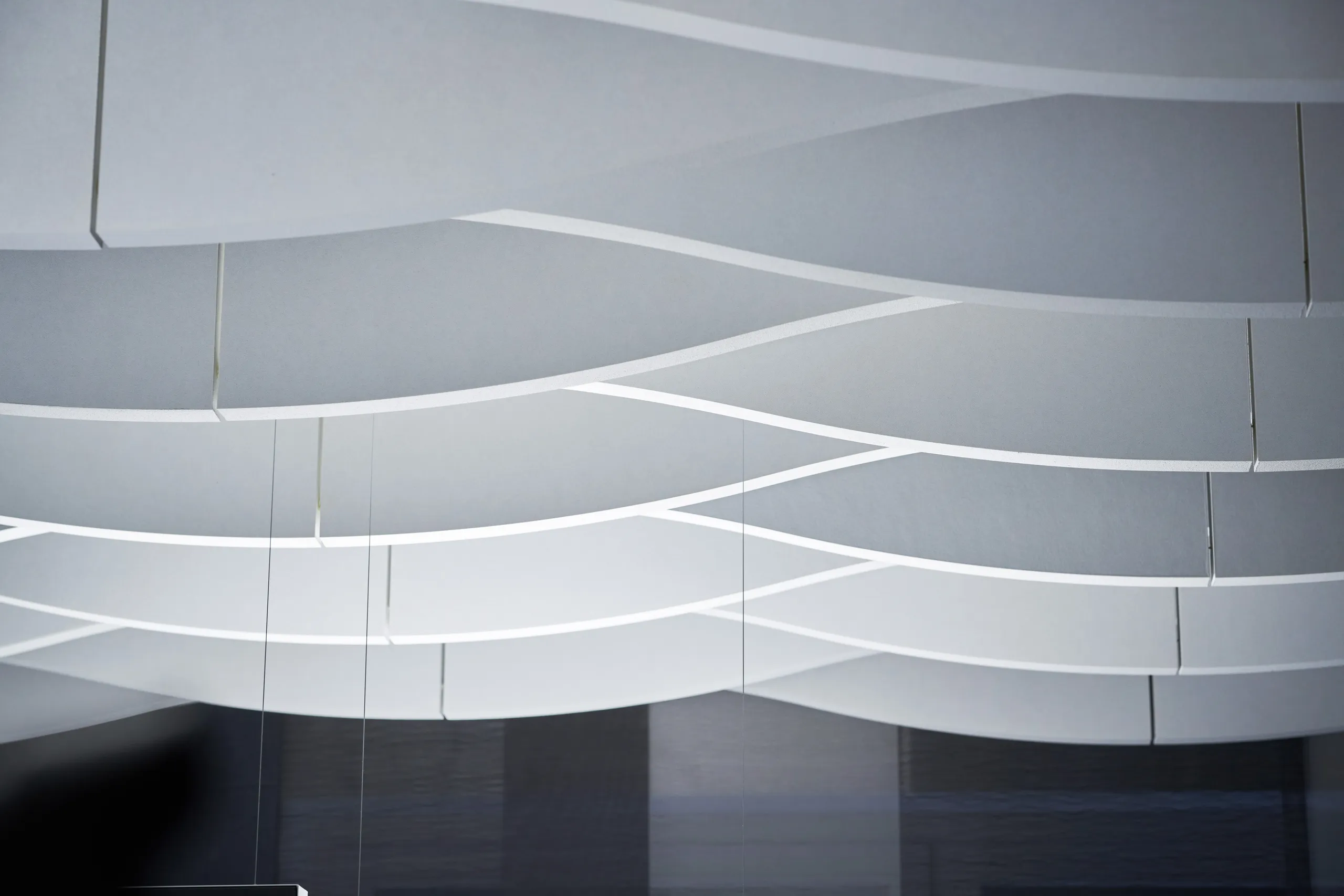 Curved, overlapping white panels create a wave-like pattern on a modern ceiling, with subtle lighting enhancing the design.