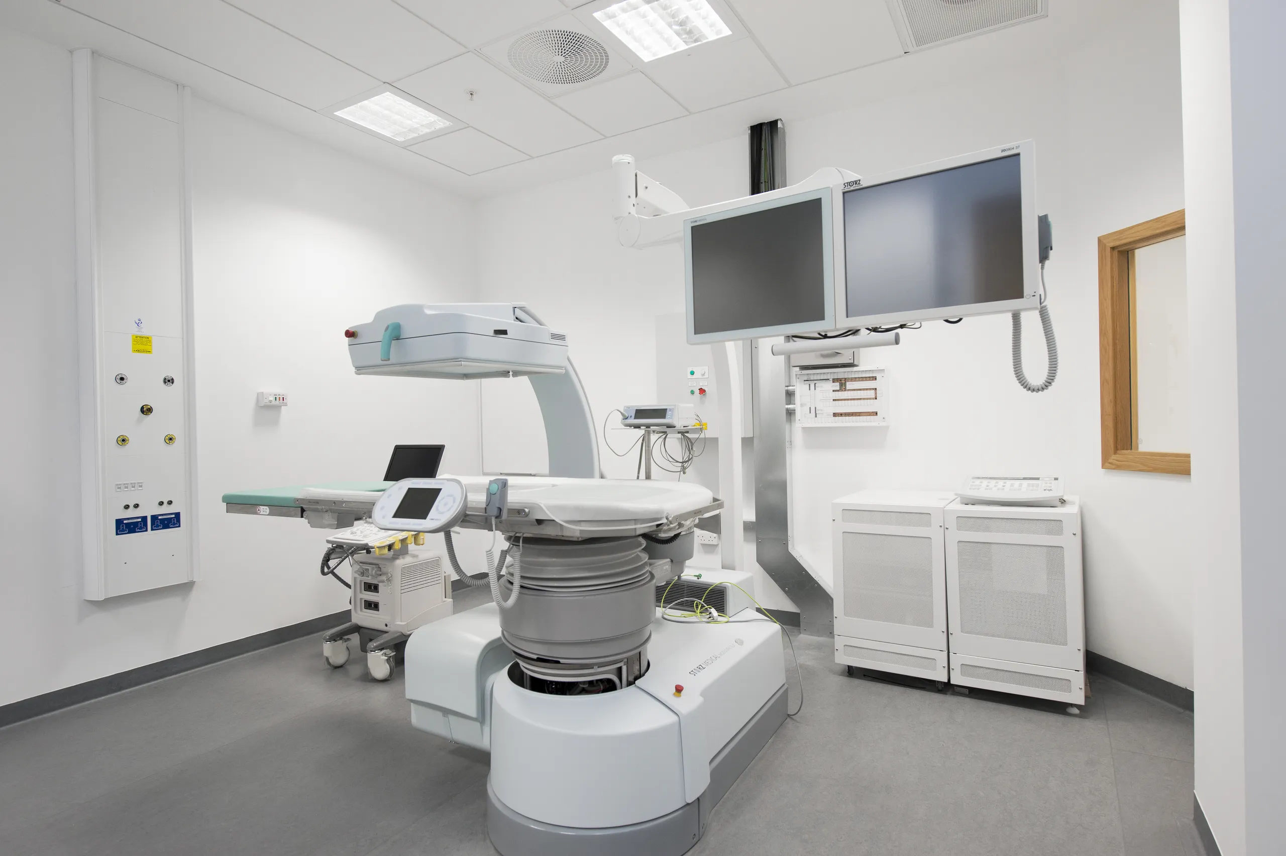 A clinical imaging suite containing advanced diagnostic equipment beneath a hygienic acoustic ceiling with integrated ventilation and lighting units.