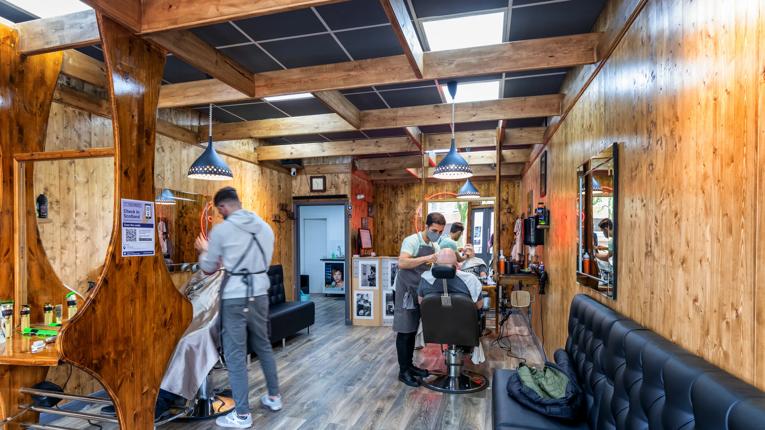 Barbershop interior with wooden walls, barber chairs, and black acoustic ceiling tiles installed between exposed timber beams.