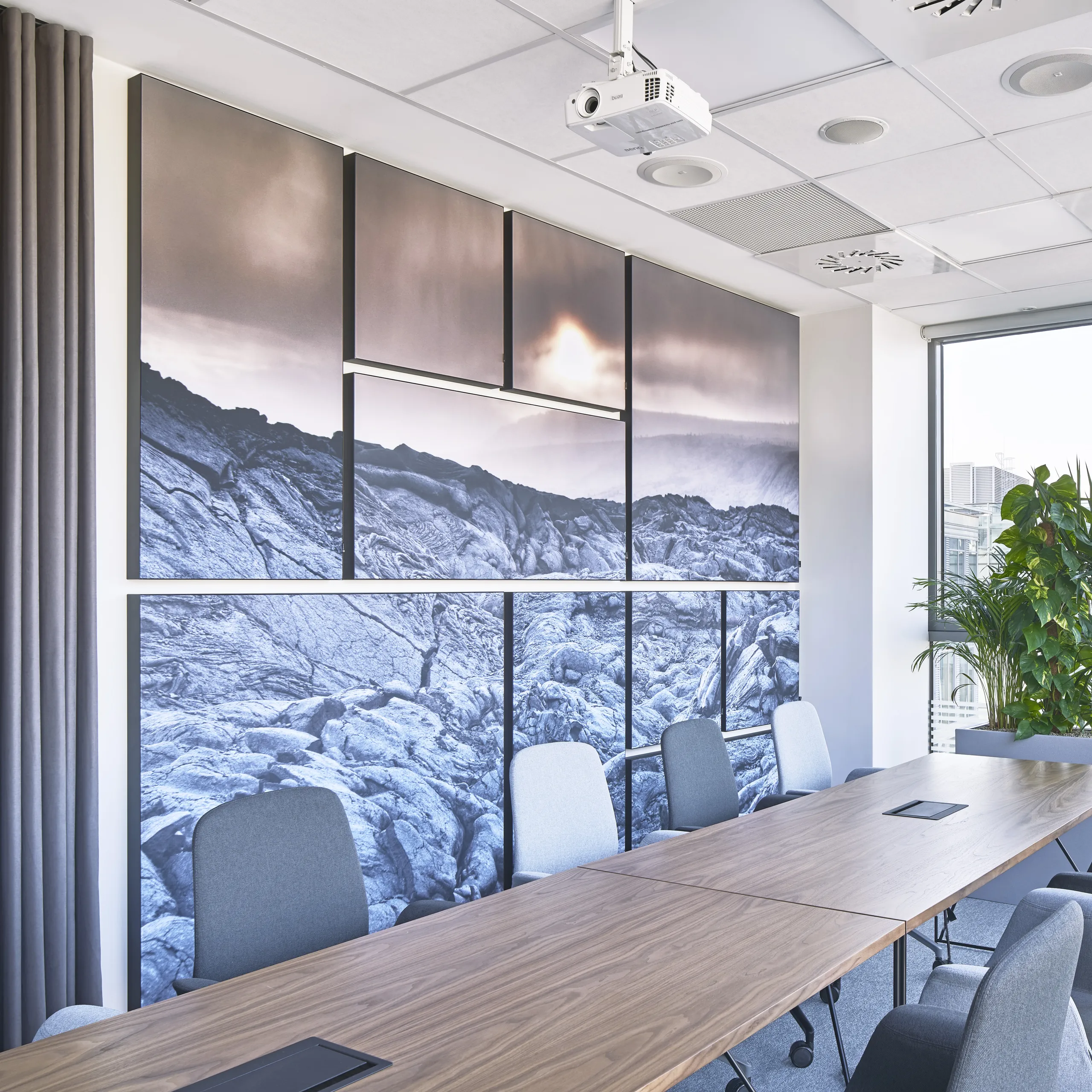 Meeting room with white acoustic ceiling panels, large photographic puzzle acoustic wall panels, a long wooden conference table, and floor-to-ceiling windows