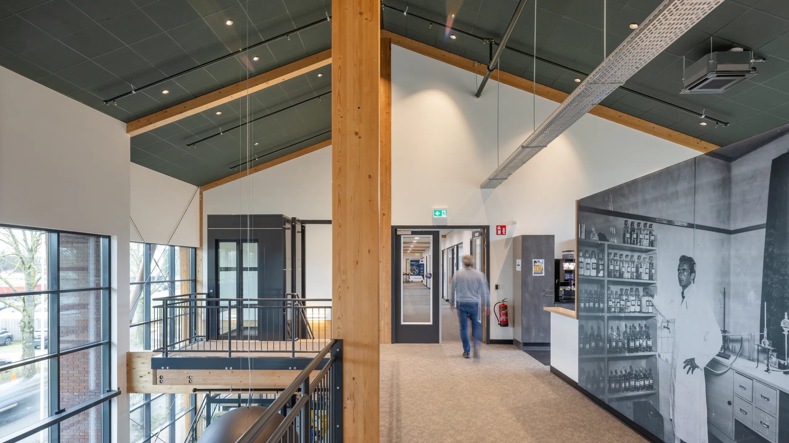 Modern interior with high ceilings, exposed wooden beams, and a large black-and-white historical photo. A person walks down the hallway.