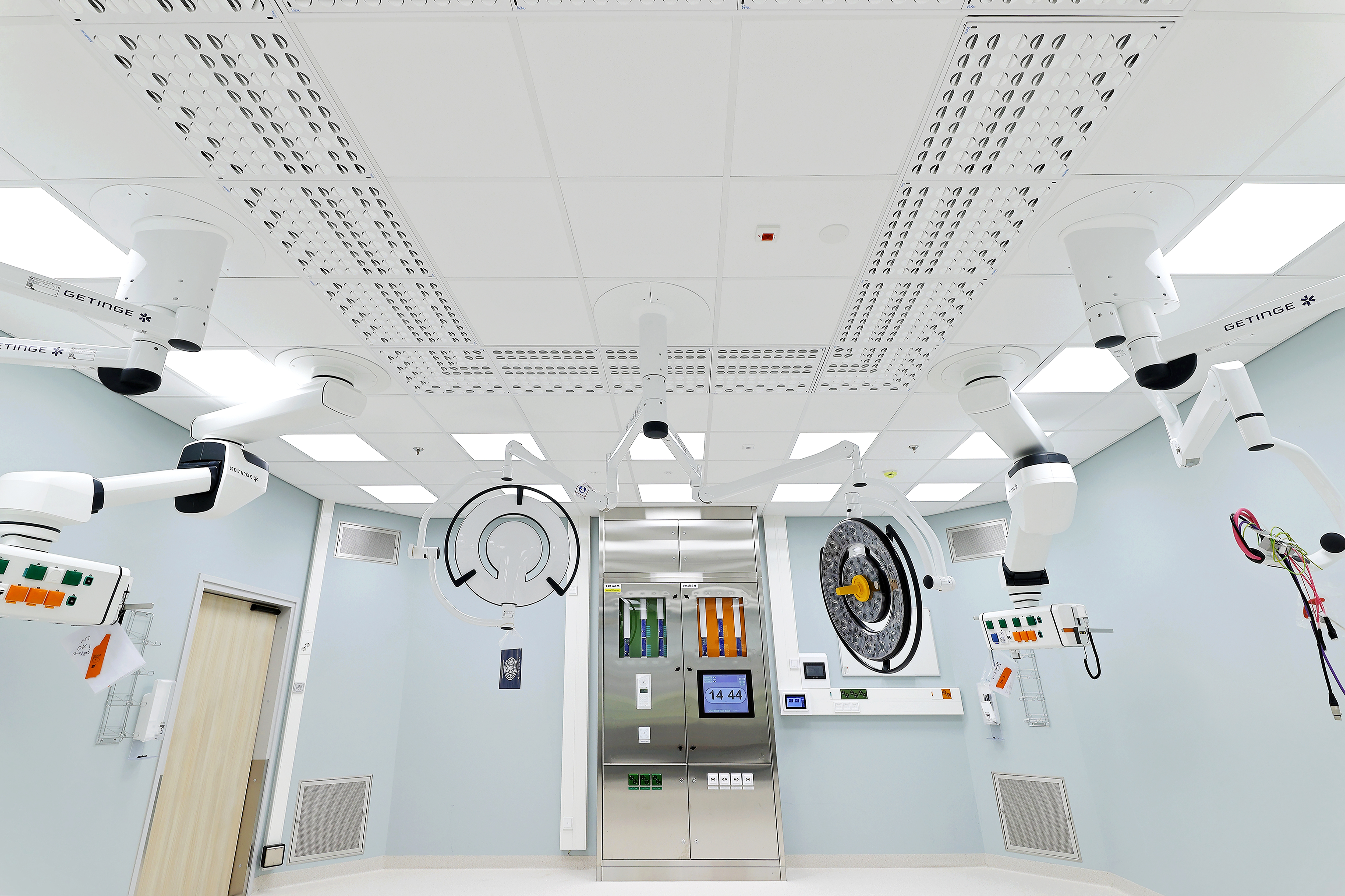 Operating theatre with a hygienic white acoustic ceiling grid, integrated medical equipment mounts and ventilation units, designed to support cleanability, noise control and clinical workflows.