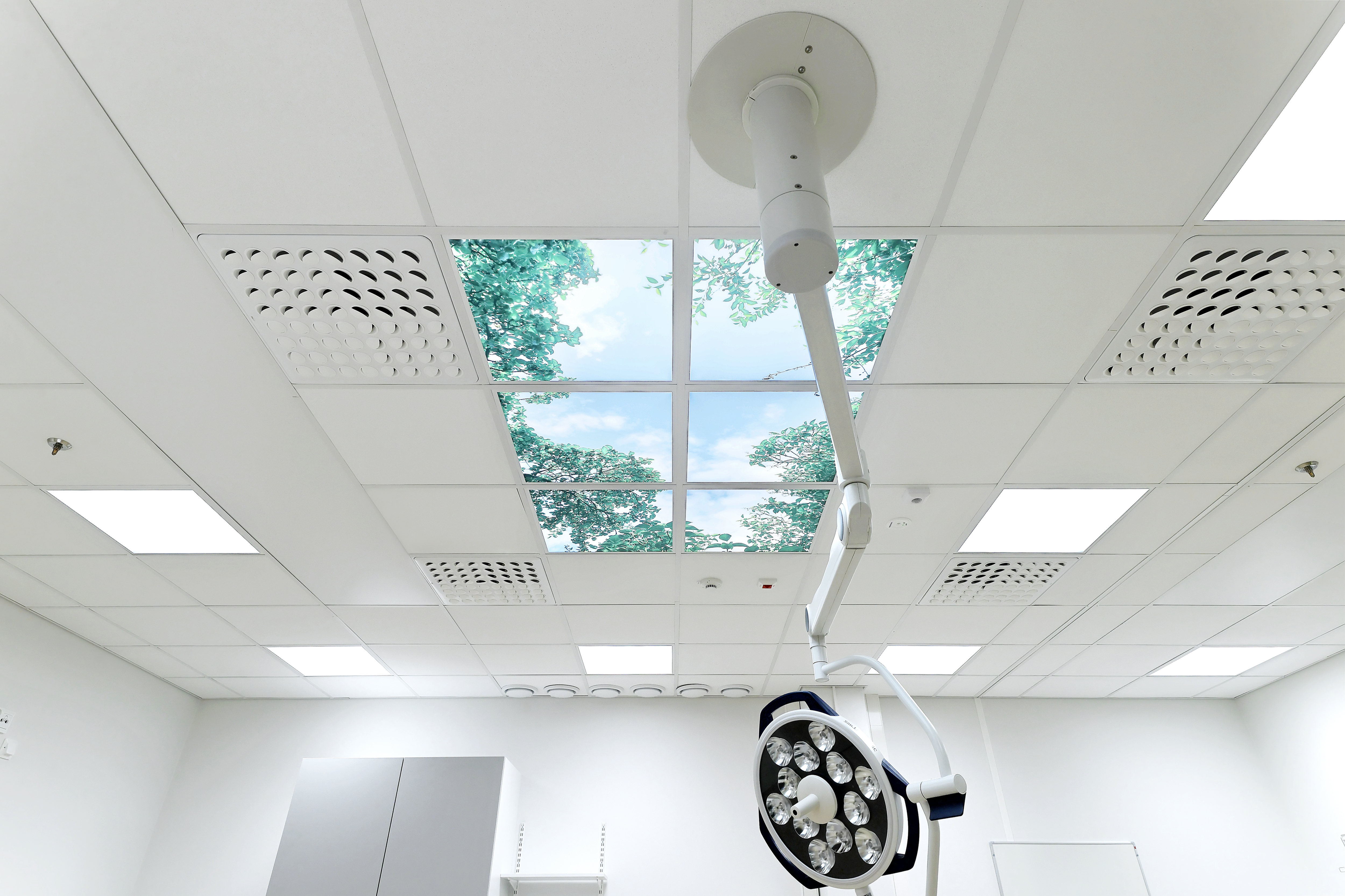 Bright surgical room featuring a smooth white acoustic ceiling with mounted operating lights and air-supply modules, providing a clean, low-noise environment for medical procedures