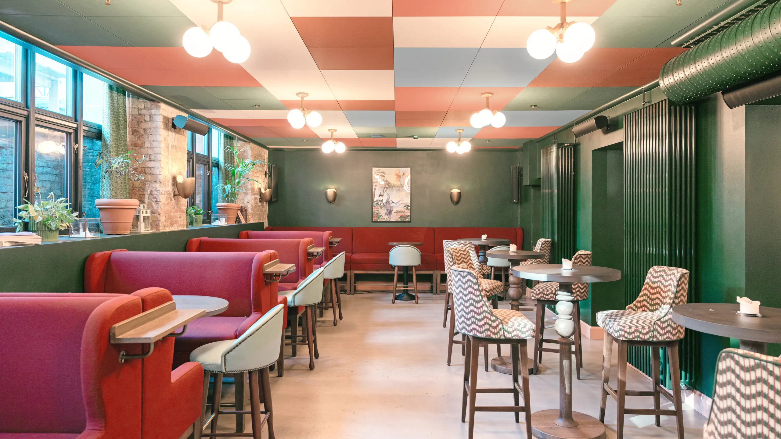Café interior with a colourful checkerboard acoustic ceiling, red booth seating, green walls, and high tables arranged along the dining area.