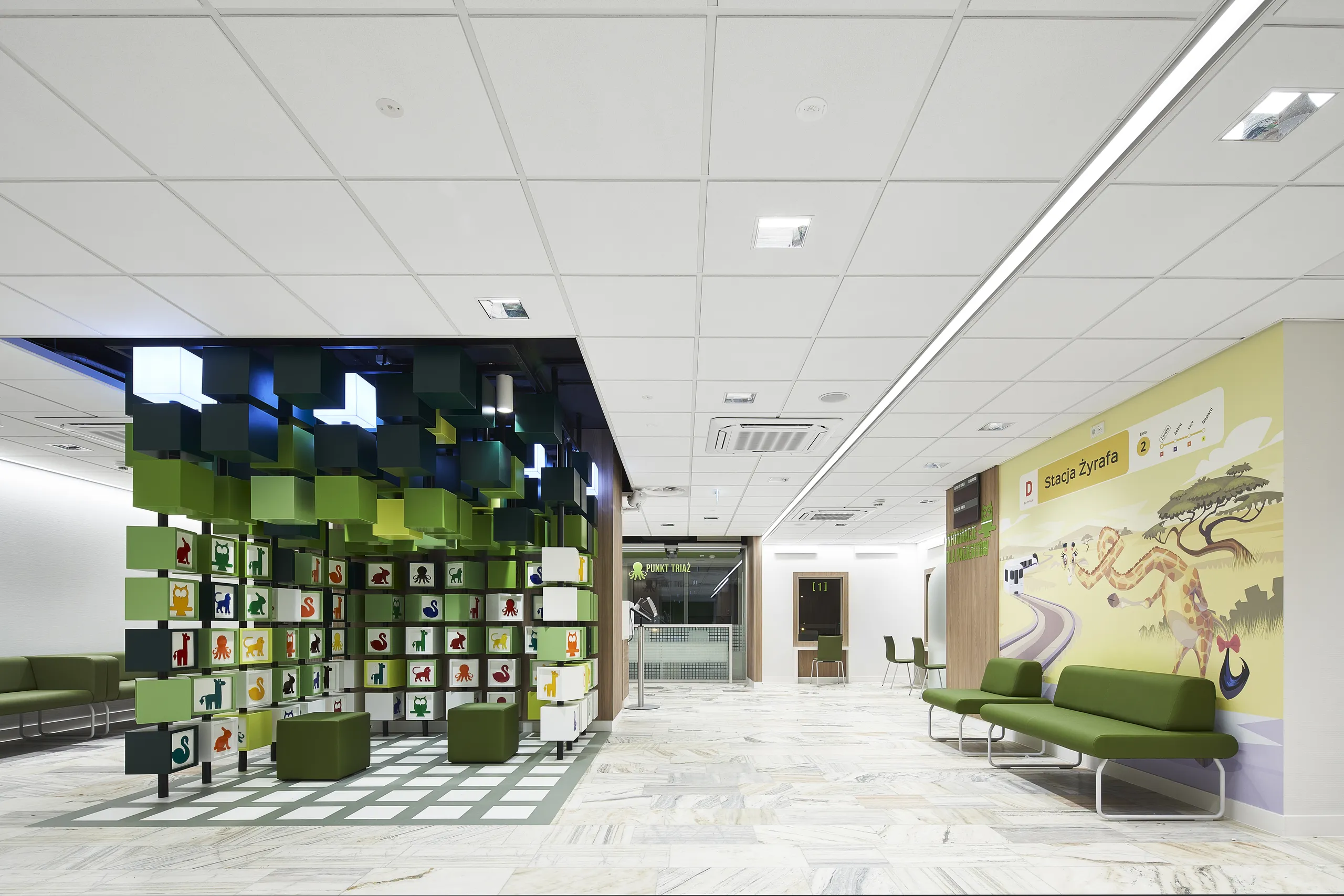 A paediatric hospital lobby with colourful cube installations, wall graphics and a white acoustic ceiling grid with integrated lighting and services.