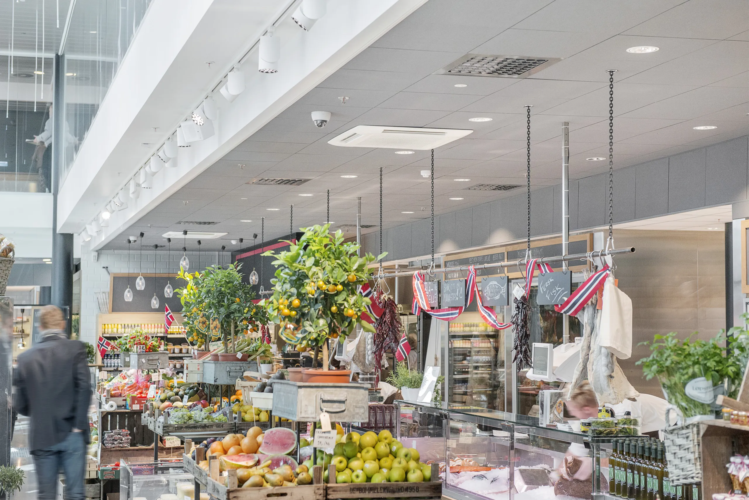 Food hall market interior with produce displays, deli counters, and a suspended acoustic ceiling system above the retail space.