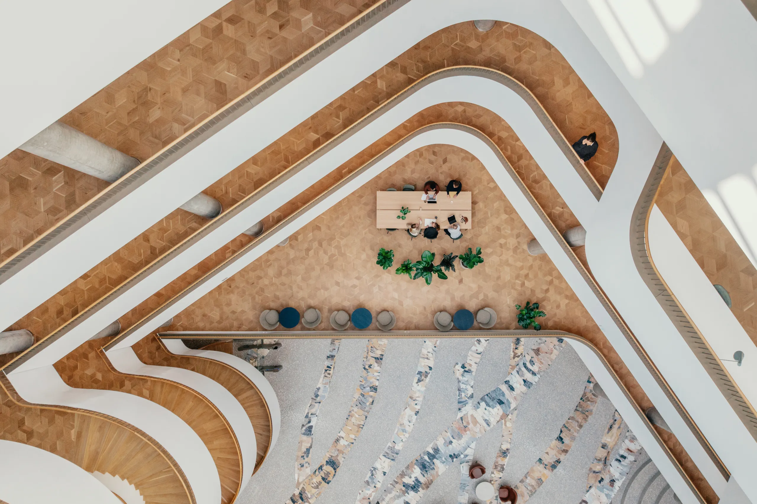 Atrium workspace with curved staircases, patterned flooring, and a person working at a desk overlooking the open interior.