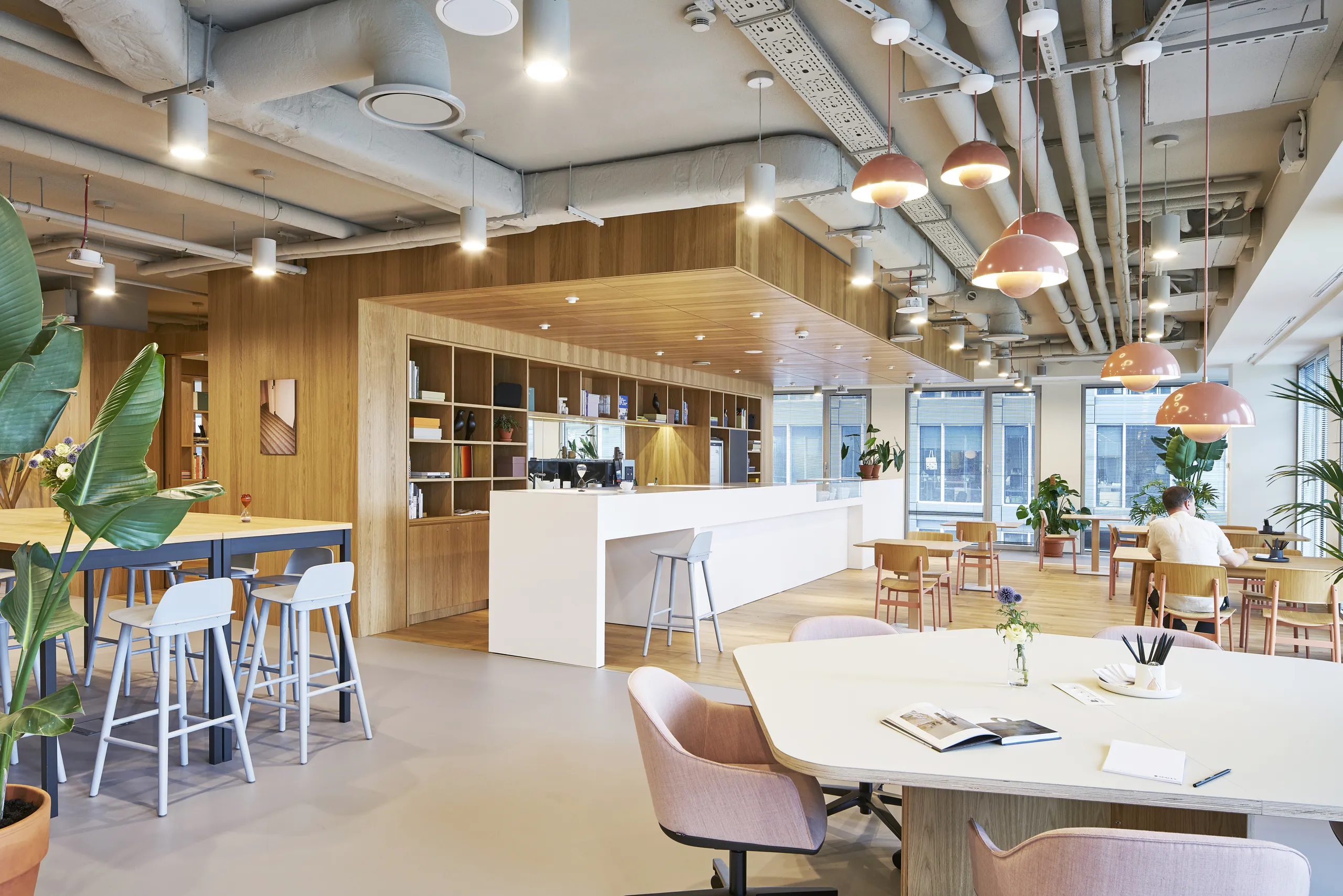 Flexible workspace with a seamless coloured monolithic acoustic ceiling above exposed services, complemented by warm timber finishes and mixed seating zones