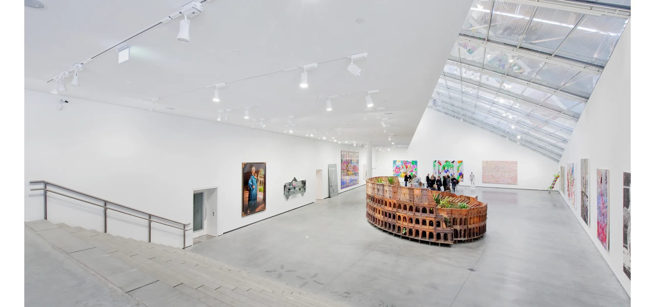 Large contemporary art gallery with a white acoustic ceiling, skylight roof section, track lighting, and colourful artworks displayed around a central sculptural installation.