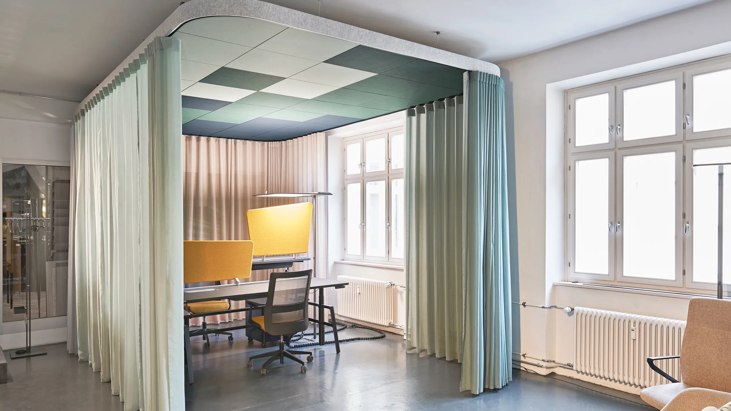 Modern office nook with green ceiling design, a table, chairs, and translucent curtains in a bright room with large windows.
