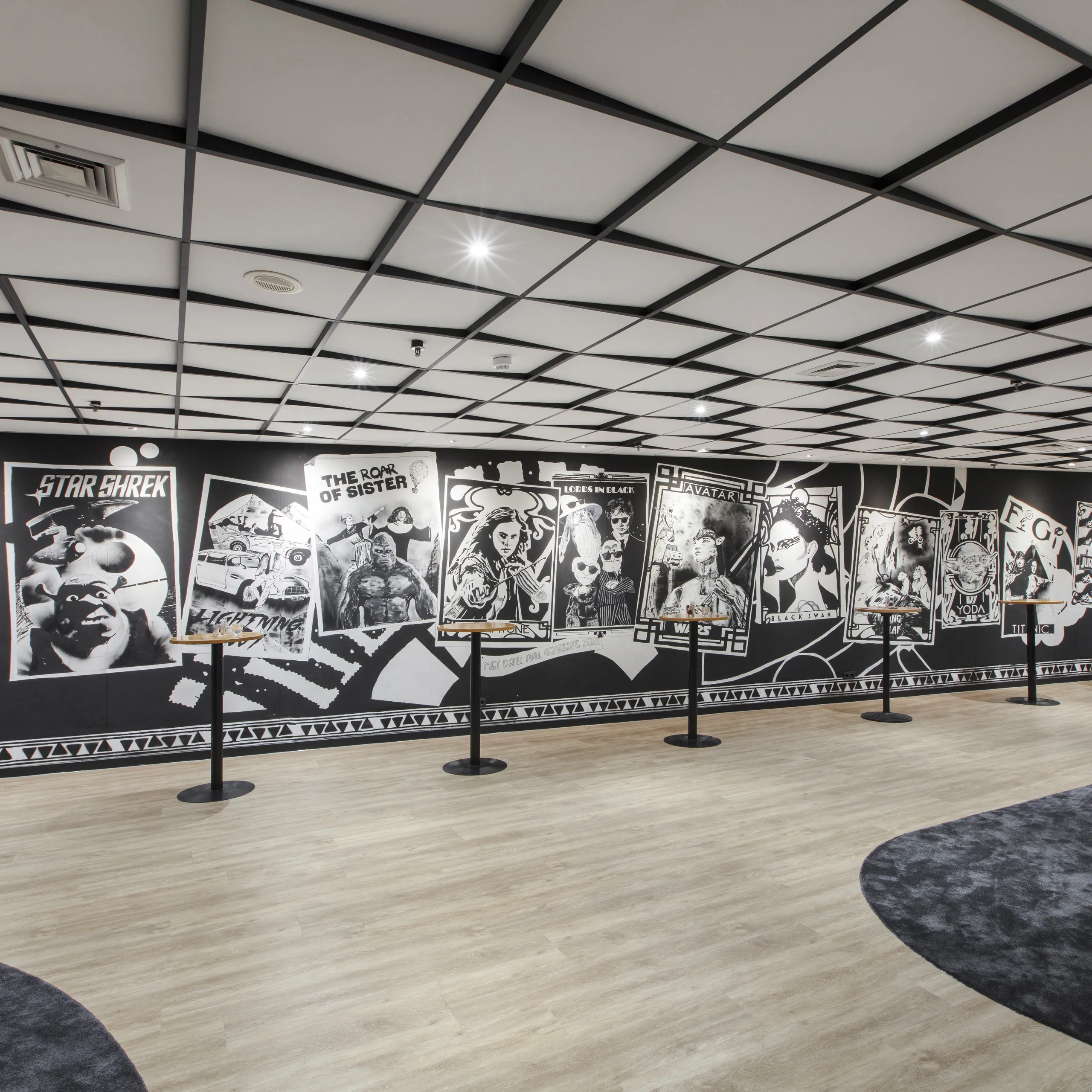 Hotel Theater Figi waiting area with graphic mural walls and a grid acoustic ceiling above the open foyer space.