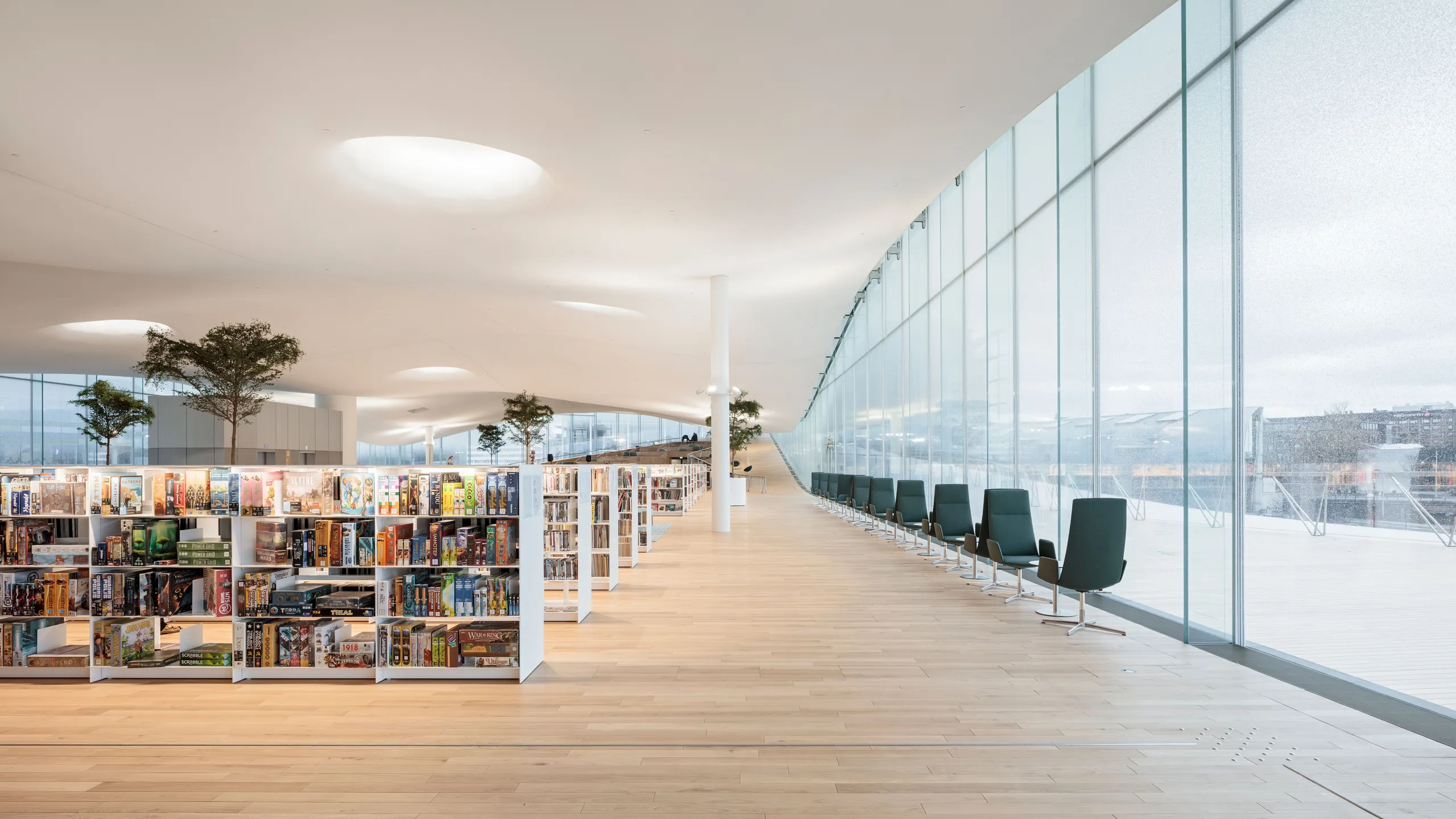 The Oodi Library’s open reading hall featuring a smooth, seamless Rockfon Mono Acoustic ceiling, with natural light flooding over bookshelves, indoor trees, and lounge seating.