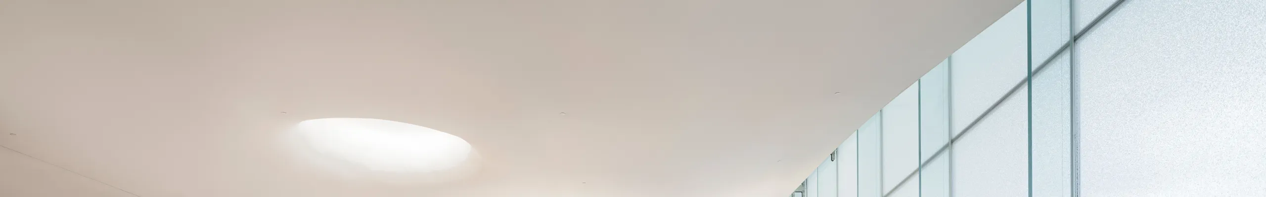 The Oodi Library’s open reading hall featuring a smooth, seamless Rockfon Mono Acoustic ceiling, with natural light flooding over bookshelves, indoor trees, and lounge seating.