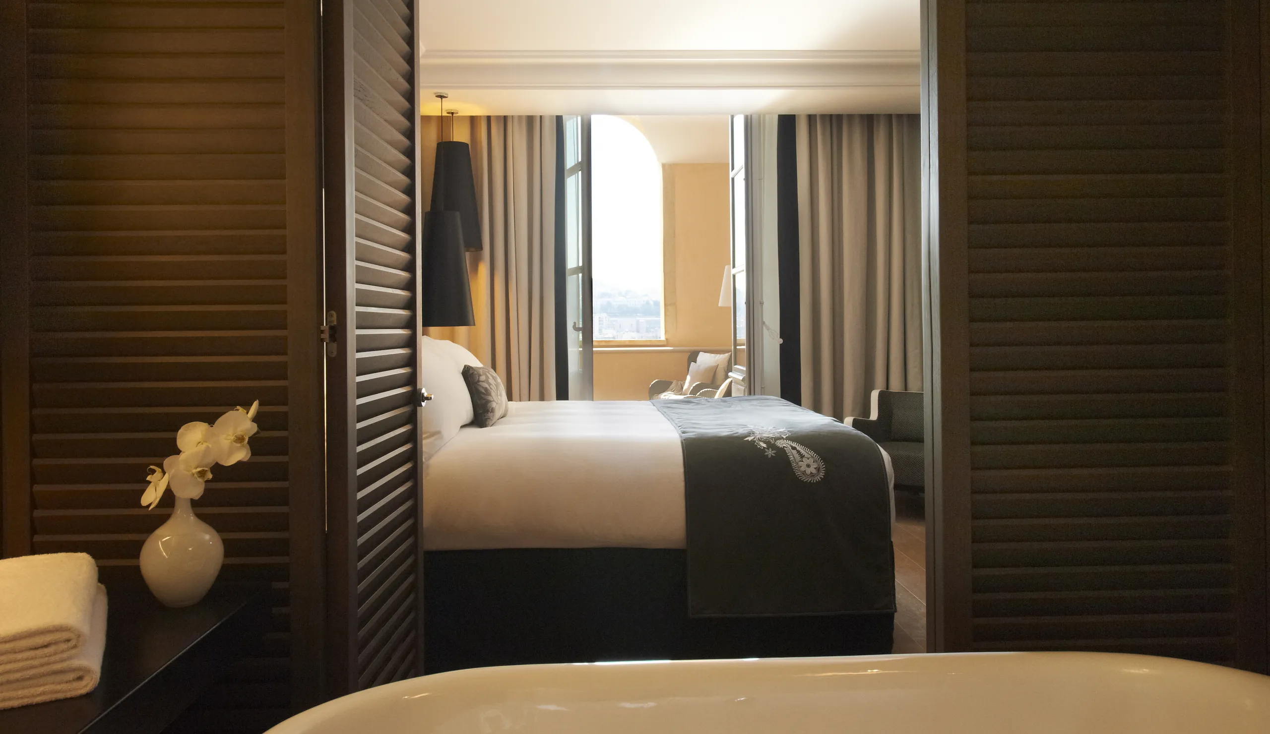 Hotel bedroom interior with a large bed, pendant lighting, and a smooth white acoustic ceiling above the room.