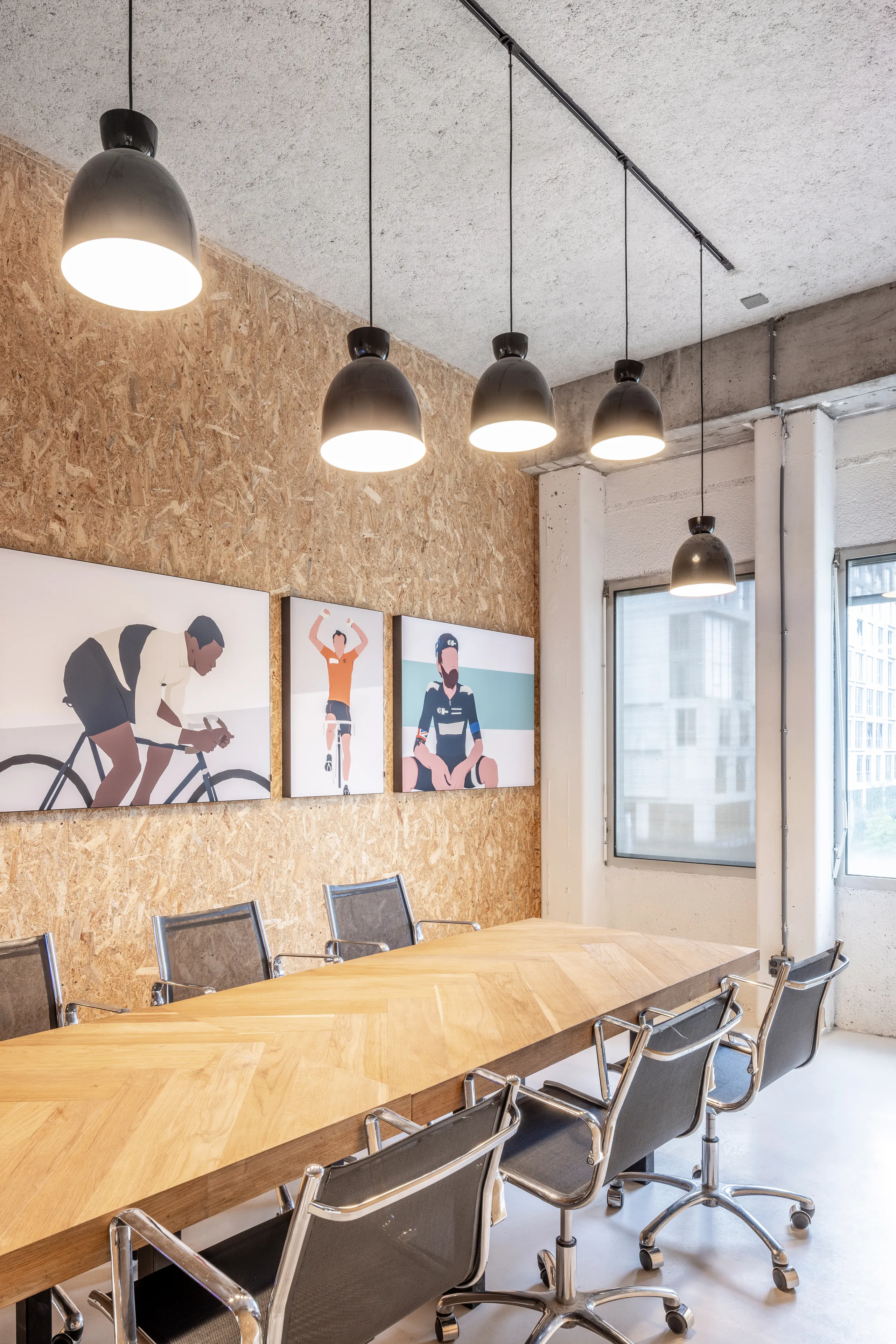 Meeting room with spray-applied acoustic ceiling absorber and acoustic wall panel, pendant lighting, and a long wooden table surrounded by black office chairs
