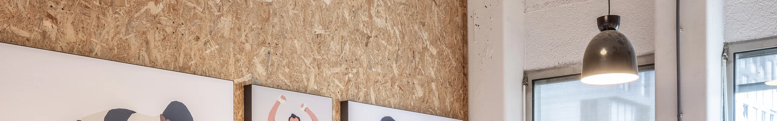 Meeting room with spray-applied acoustic ceiling absorber and acoustic wall panel, pendant lighting, and a long wooden table surrounded by black office chairs
