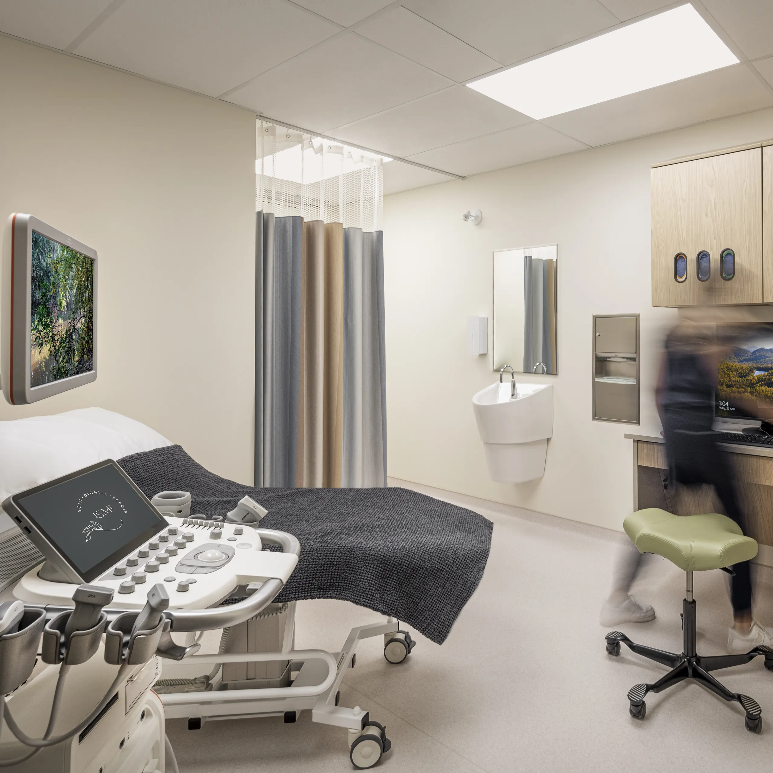 A modern ultrasound room with an examination bed, workstation and overhead acoustic ceiling panels providing bright, even lighting.